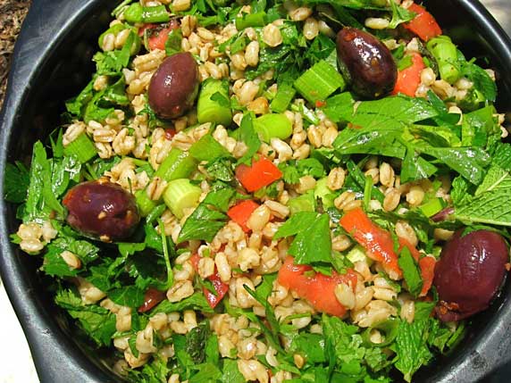 A black bowl featuring barley, kalamata olives, and lots of green herbs.