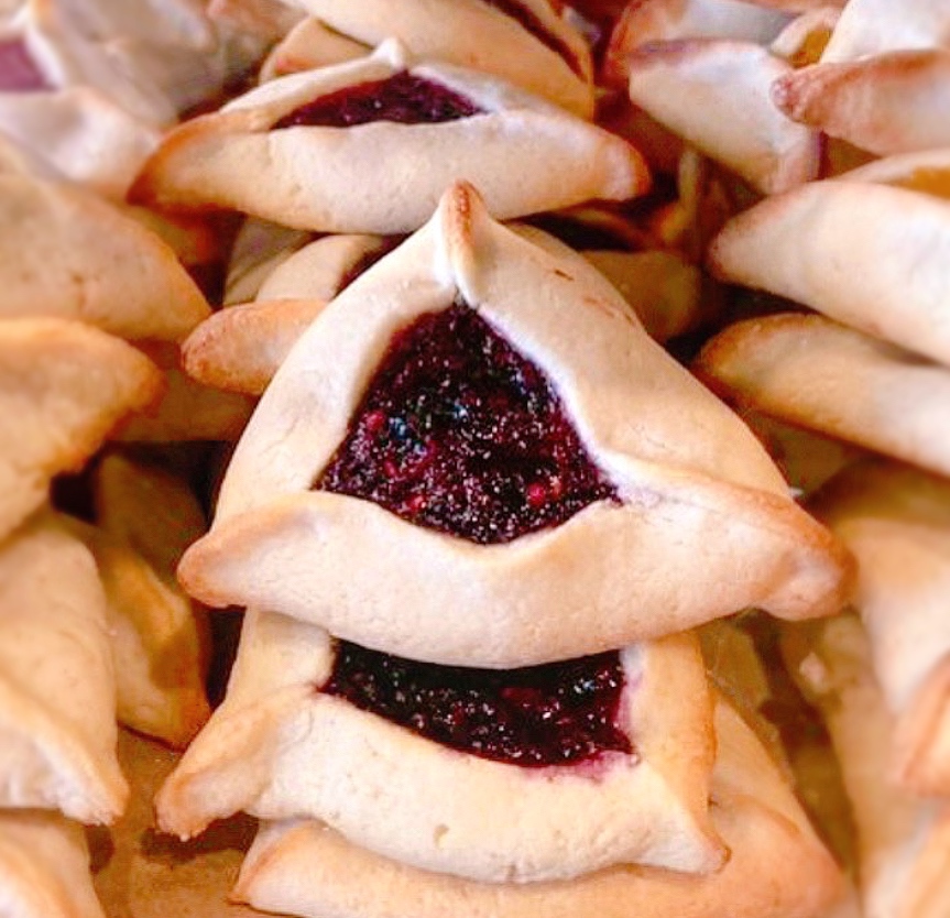 A closeup of a pile of tri-pointed pastries known as hamantaschen, with dark berry filling.