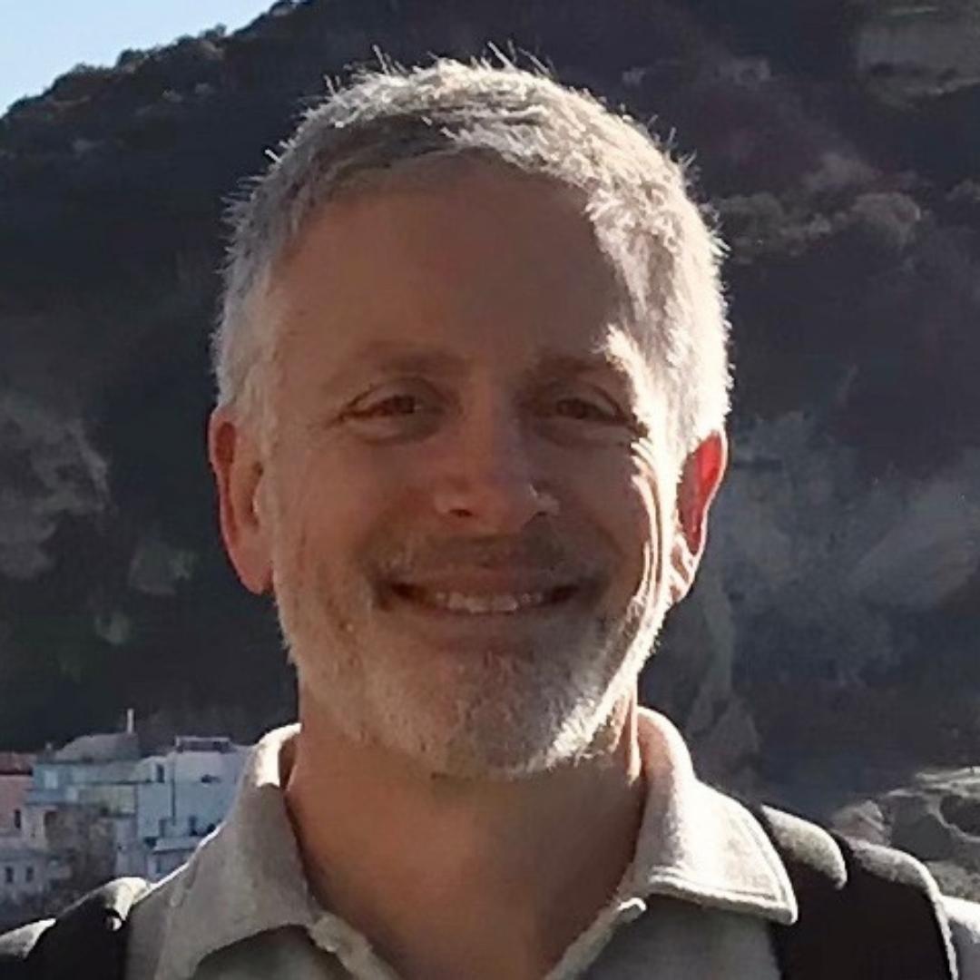 Jeff Schraeger, smiling in front of mountains and wearing a gray collared shirt.