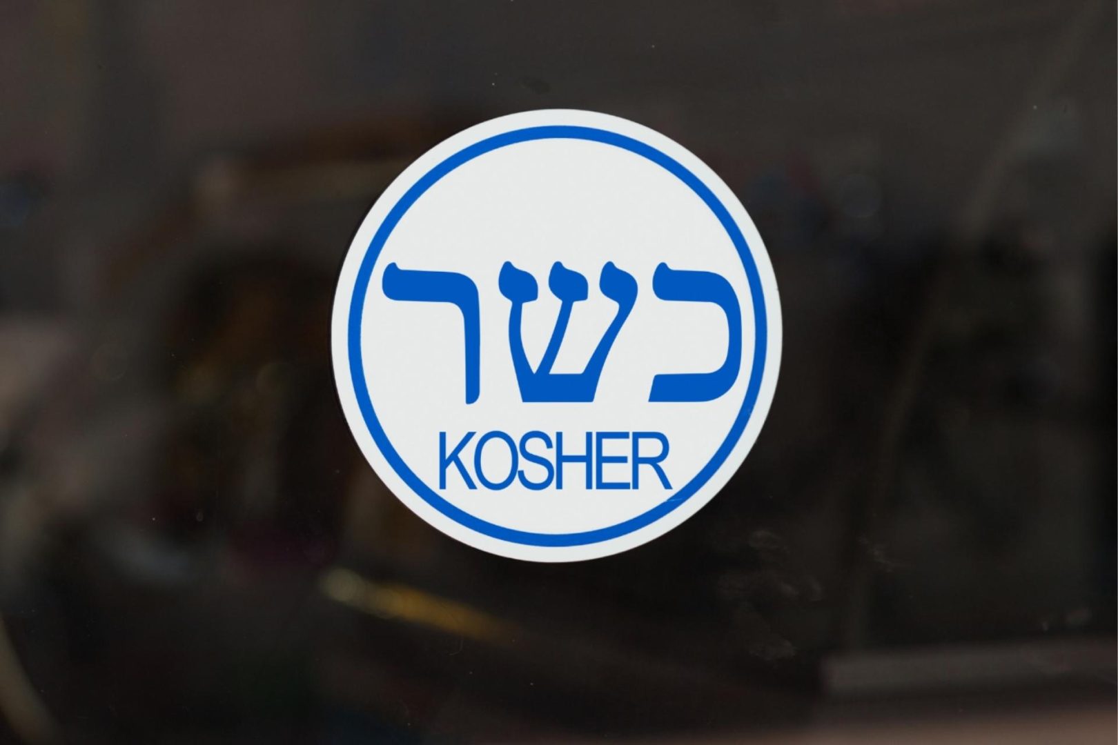 Blue text featuring the Hebrew word for Kosher and the word Kosher written out inside a white circle with a dark background around it.