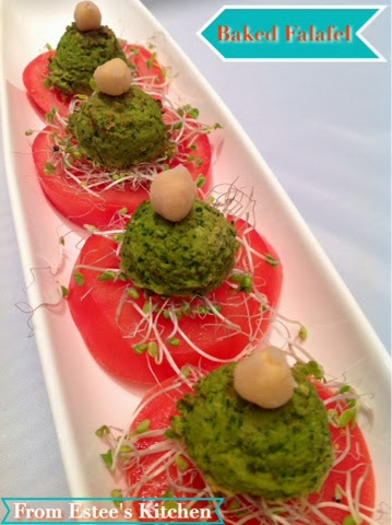 A long rectangular white plate featuring tomato slices topped with green falafel spheres topped with chickpeas and broccoli sprouts.