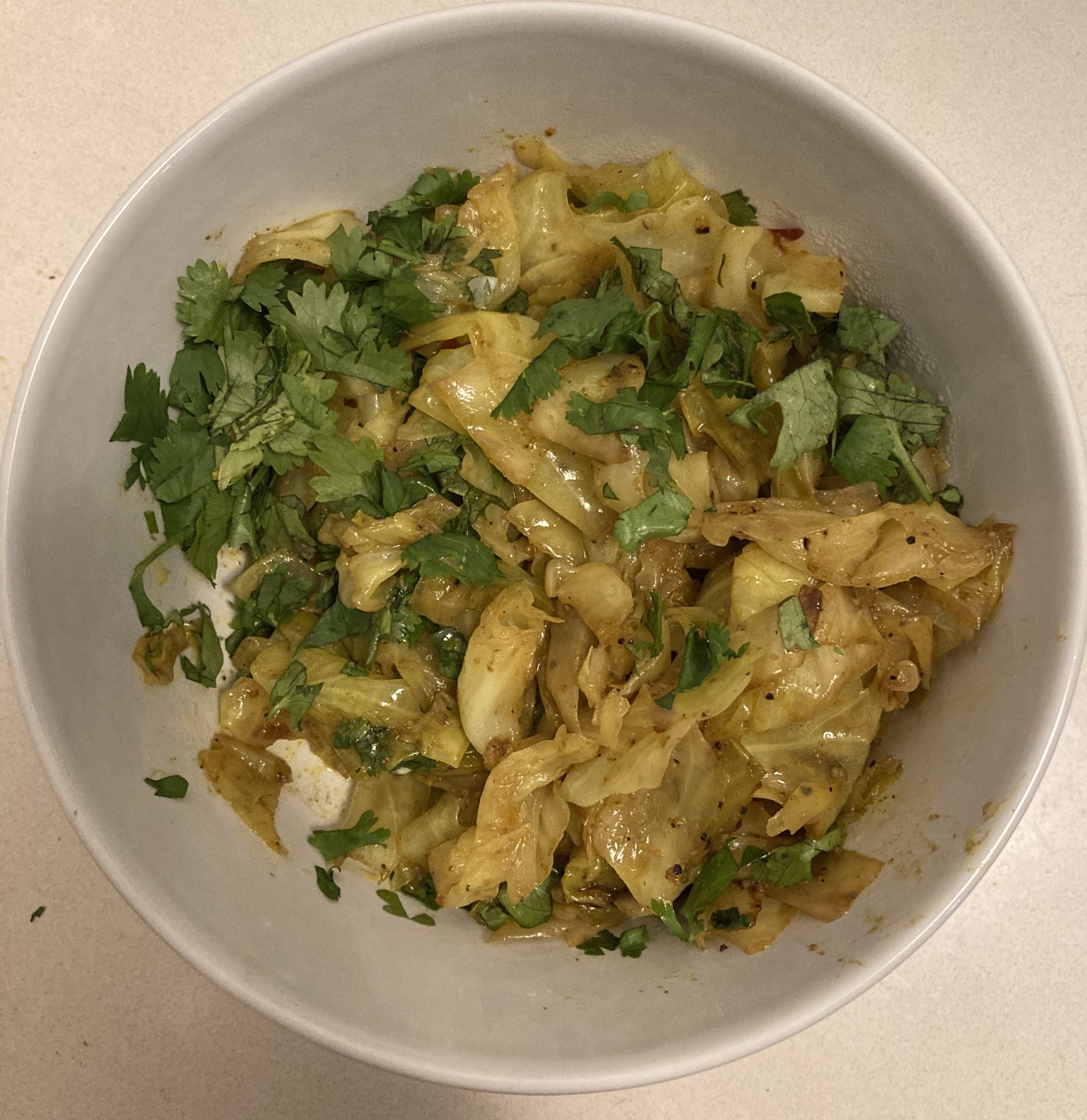 A white bowl of sauteed cabbage and cilantro on a white counter.