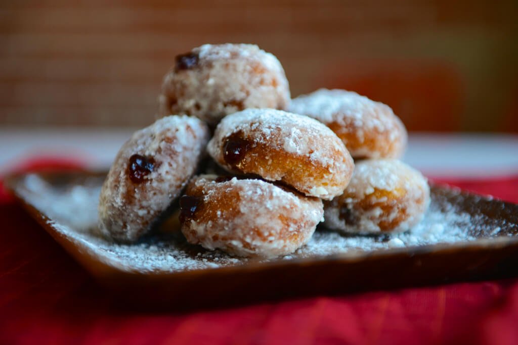 A square brown platter topped with sufganiyot--raspberry jelly filled donuts topped with powdered sugar, all on a red tablecloth.