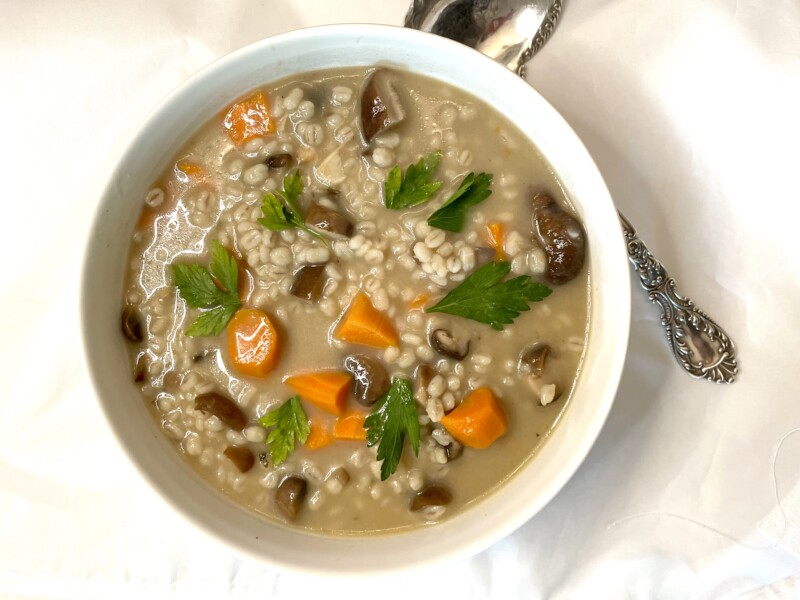 A white bowl filled with barley soup with chunks of carrot, mushroom, and sprigs of parsley.