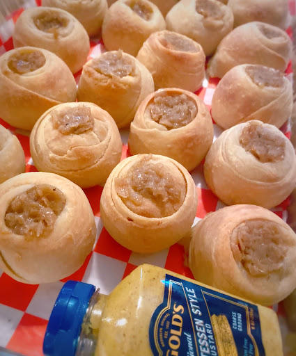 Small round cooked balls of dough filled with brown caramelized onion mixture on a red checkerboard table next to a bottle of Gold's mustard.